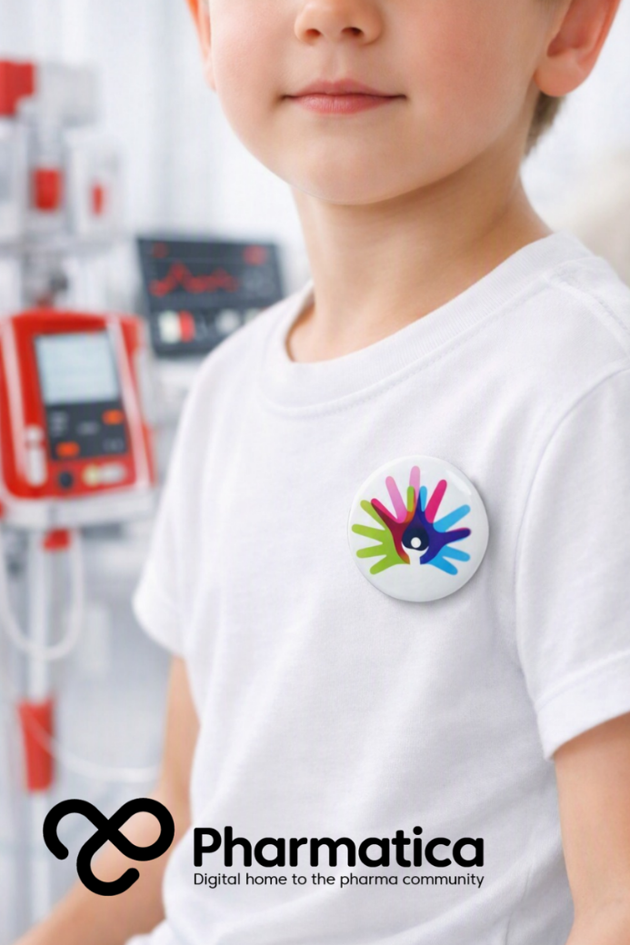 Pharmatica close-up image of a young child wearing a white T-shirt with a Rare Disease Day badge, seated in a bright clinical home environment with red medical devices in the background, representing rare disease care, patient independence, and humanitarian medical technology.