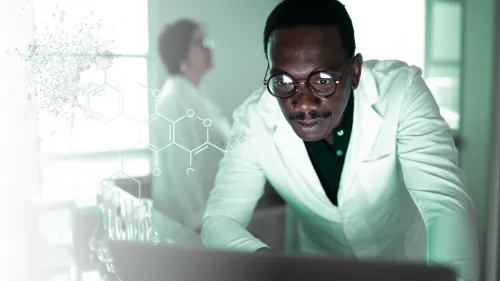 A focused scientist with glasses and a white lab coat leans over a laptop in a bright laboratory. On the left, a transparent chemical molecular structure diagram overlays a faint view of lab glassware, while another colleague is visible in the background.